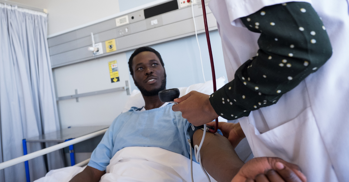 black man in hospital bed getting blood pressure checked