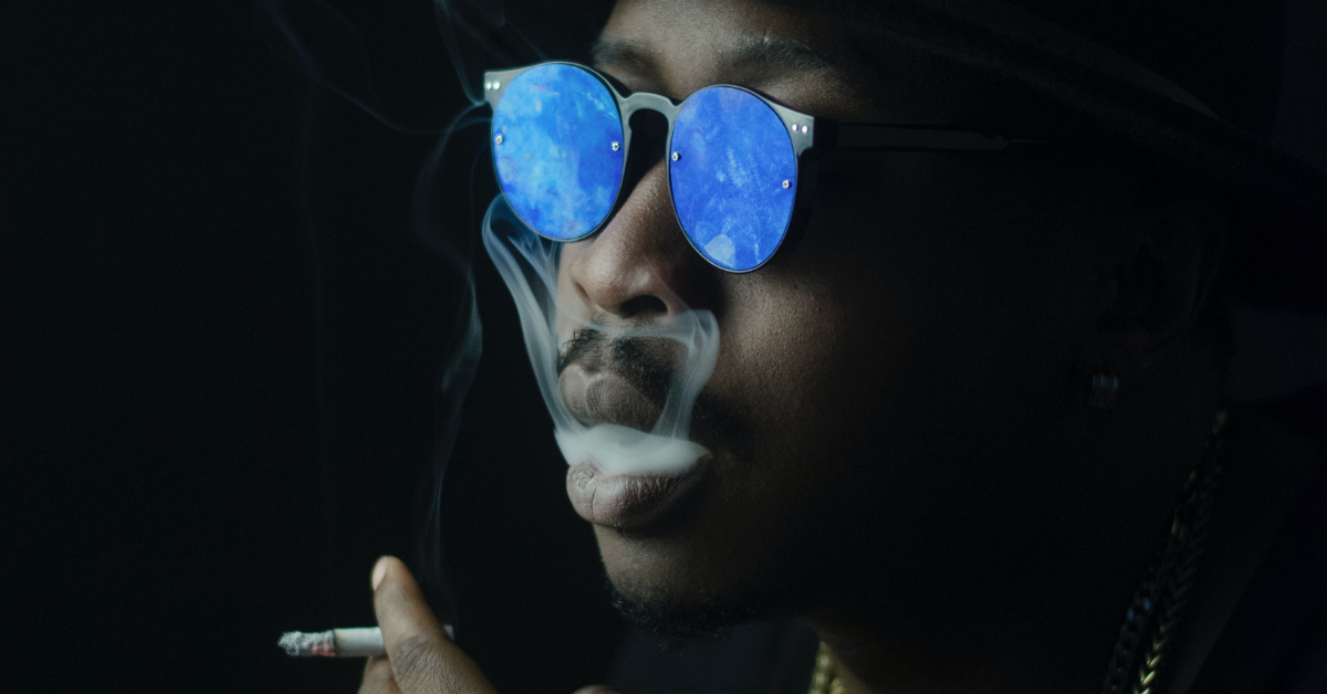 A black man in shades smoking a cigarette